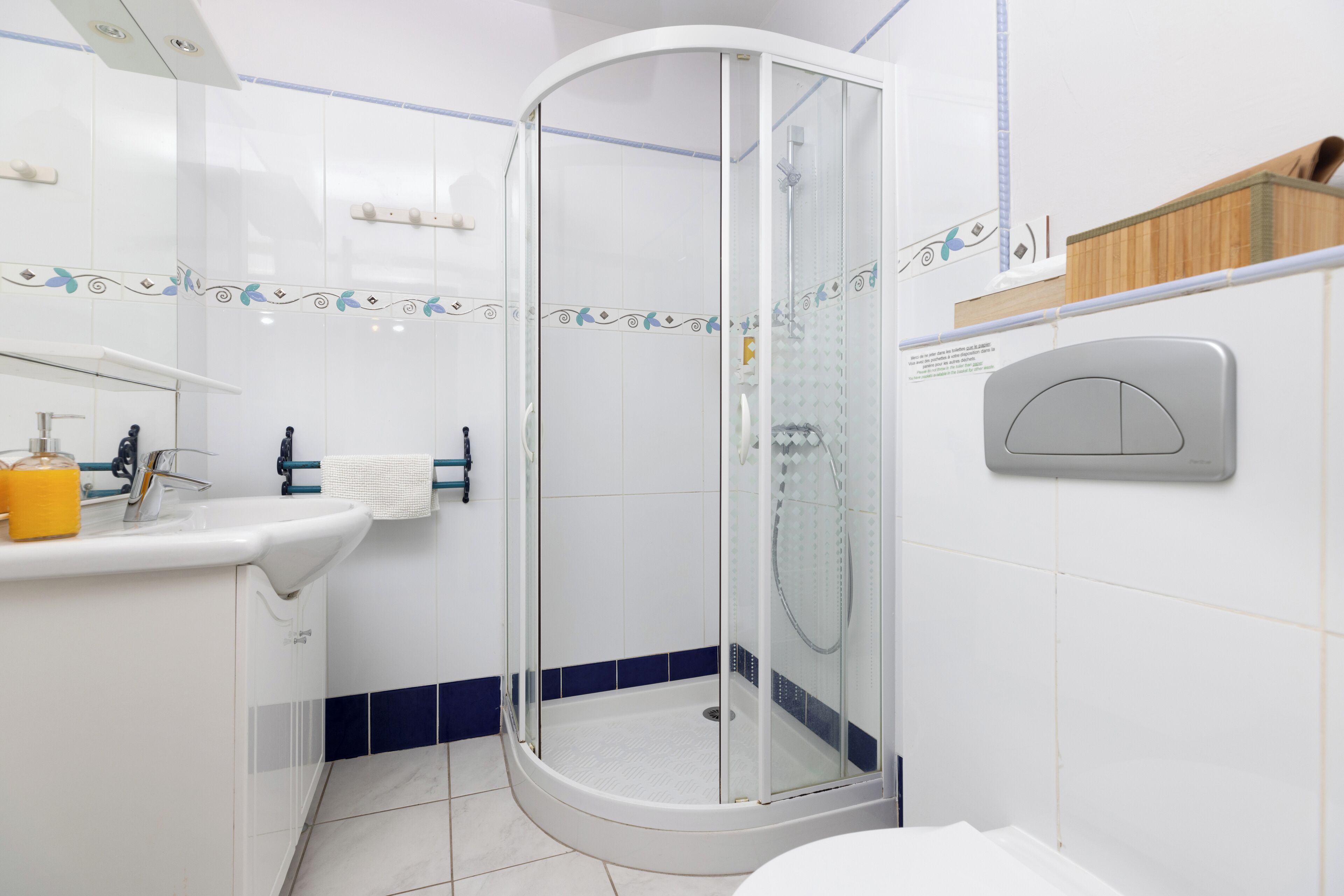 A modern bathroom with a glass-enclosed shower, a white sink with a yellow soap dispenser, and a white toilet.