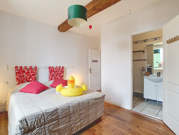 Une chambre à coucher avec un lit, une fenêtre, une porte et une salle de bain visible à travers une porte ouverte.