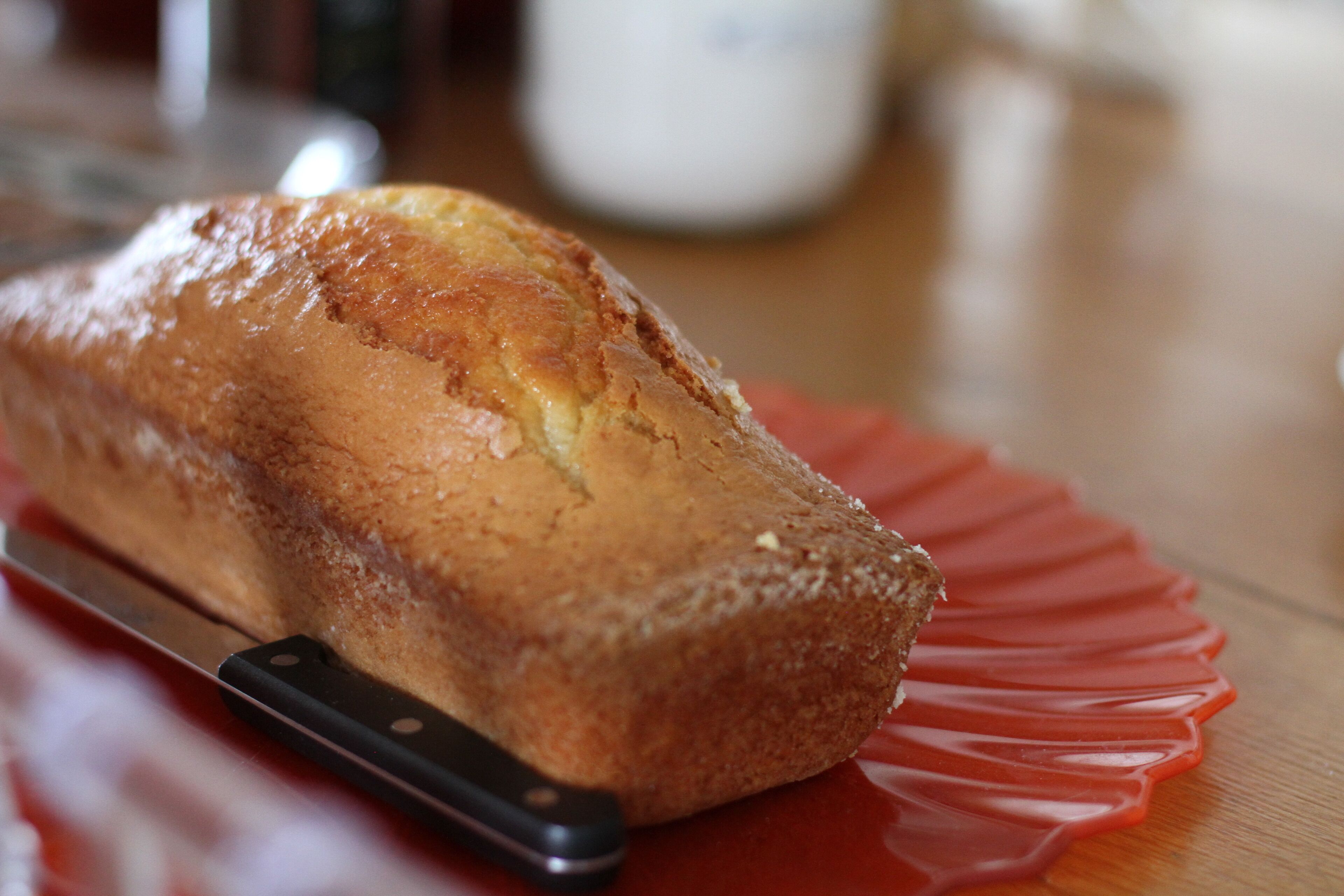 A loaf of bread on a red plate with a knife beside it.