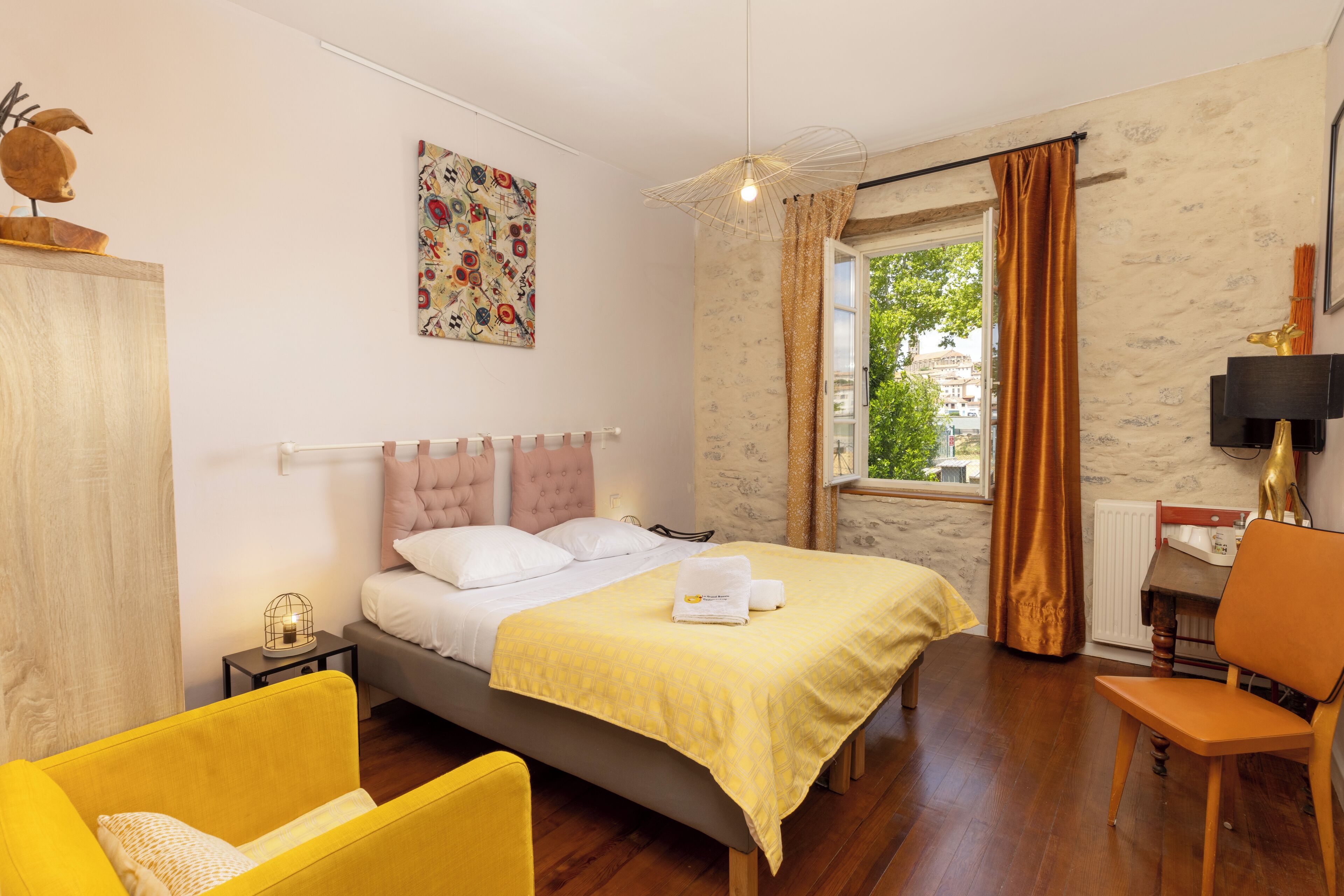 Une chambre à coucher comprenant un lit, une chaise, un bureau, une fenêtre avec des rideaux, un radiateur et un mur orné d’un élément décoratif.