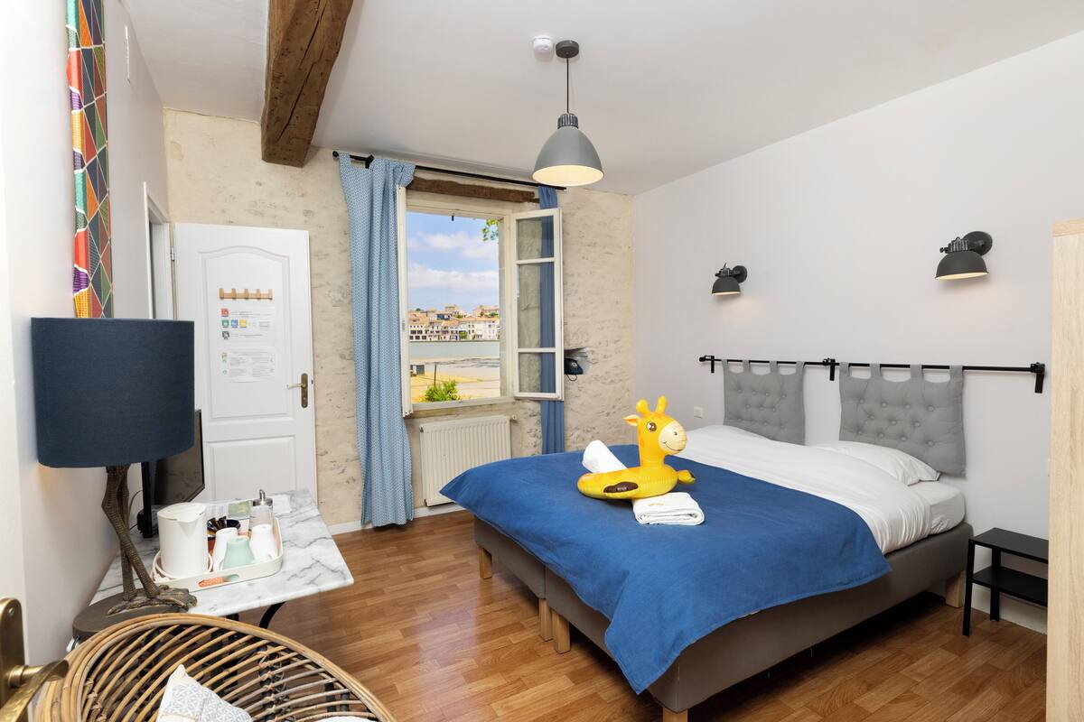 A bedroom with a bed, a desk, a chair, a window with a view, and a hanging light fixture.