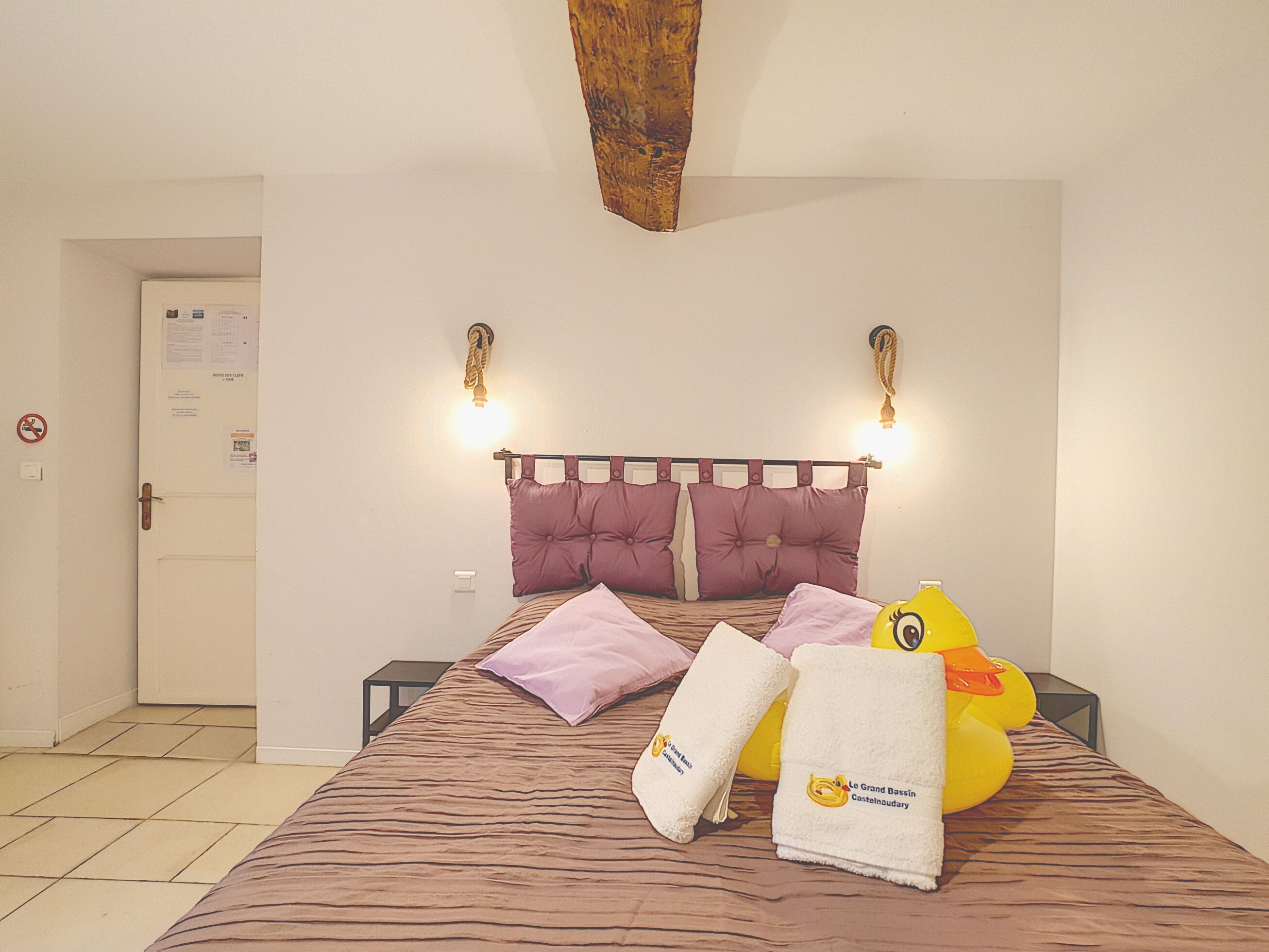 A hotel room with a bed, pillows, a yellow duck decoration, and towels.