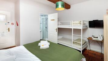 Una camera da letto con un letto a castello, una coperta verde, una porta bianca, una trave in legno al soffitto, una televisione e un tavolino con un bollitore.