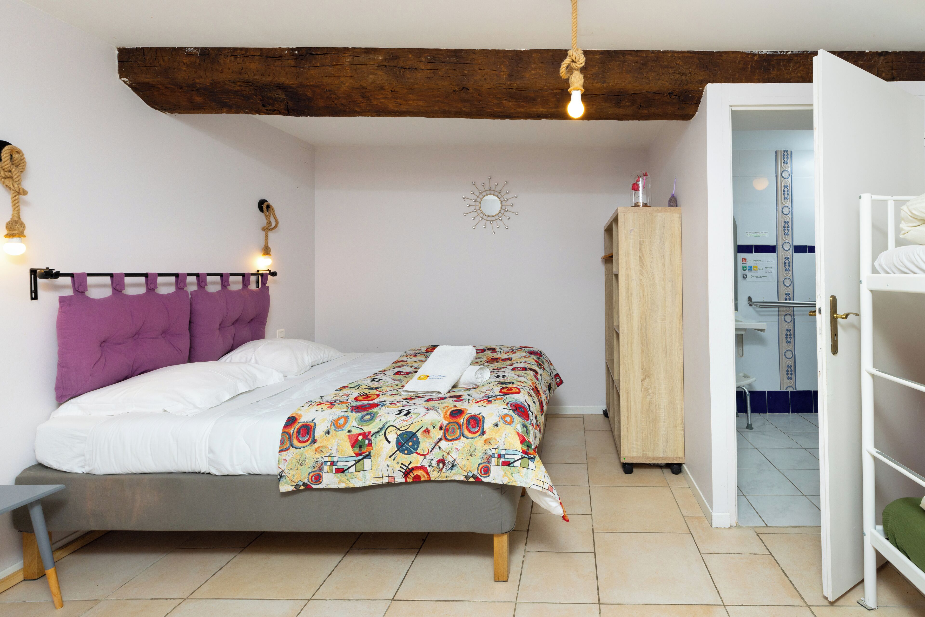 Un dormitorio con una cama, cabecera de madera, un armario y un baño visible a través de una puerta abierta.