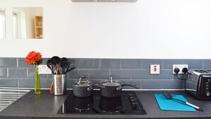 A modern kitchen with a black stovetop, two pots, a toaster, and a blue cutting board. - No 40, 5 beds, sleeps 7 (Coventry)