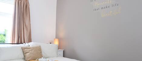 Una cama bien hecha con una bandeja de desayuno, una lámpara de noche y una pared con una frase inspiradora.