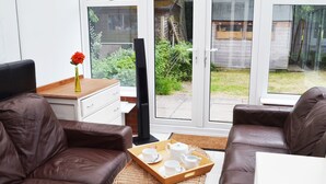 A modern living room with leather sofas, a coffee table with tea set, and large windows offering a view of a backyard. - No 40, 5 beds, sleeps 7 (Coventry)