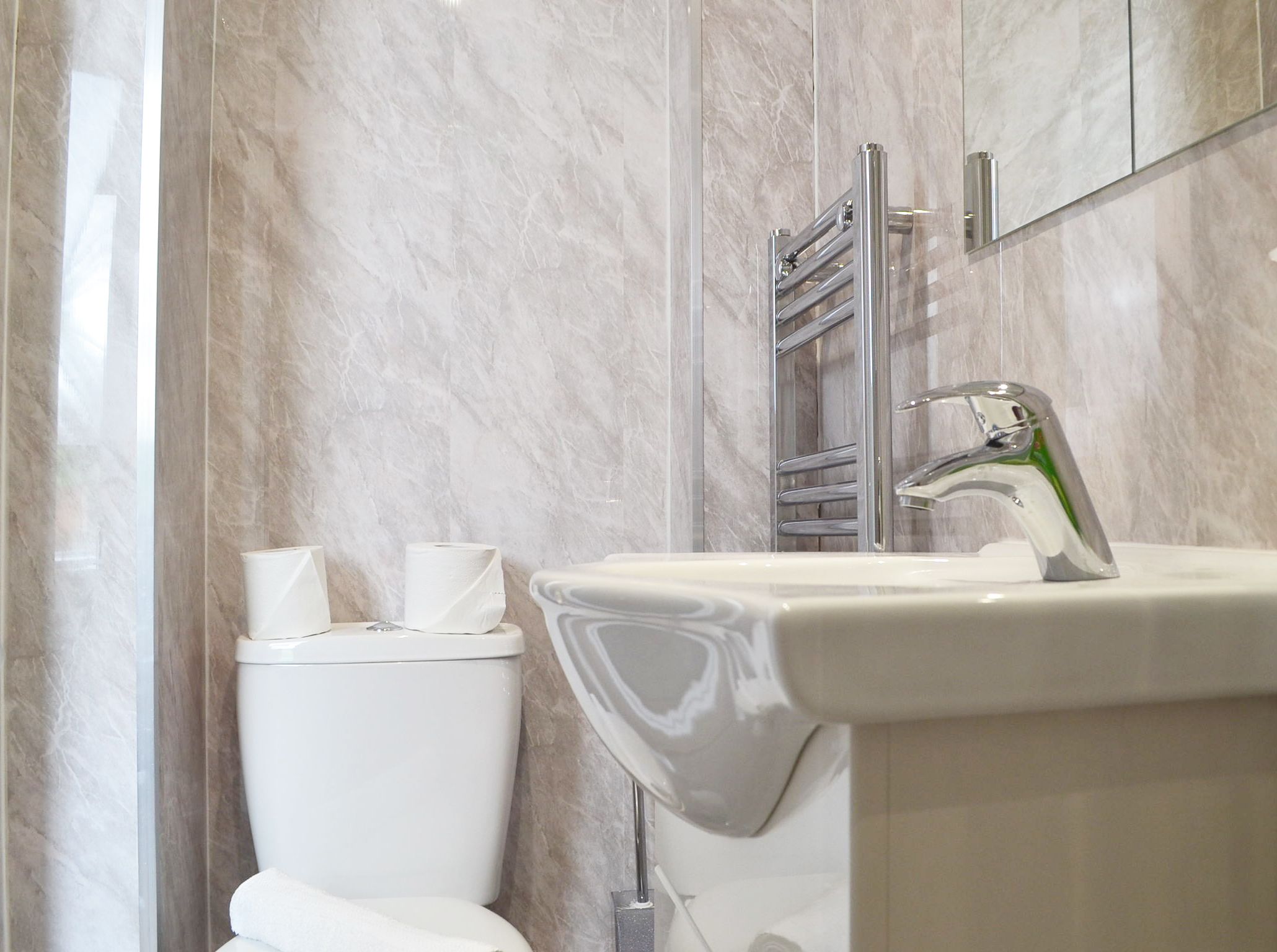 A modern bathroom with a marble wall, a white toilet, a sink with a chrome faucet, and a towel rack.