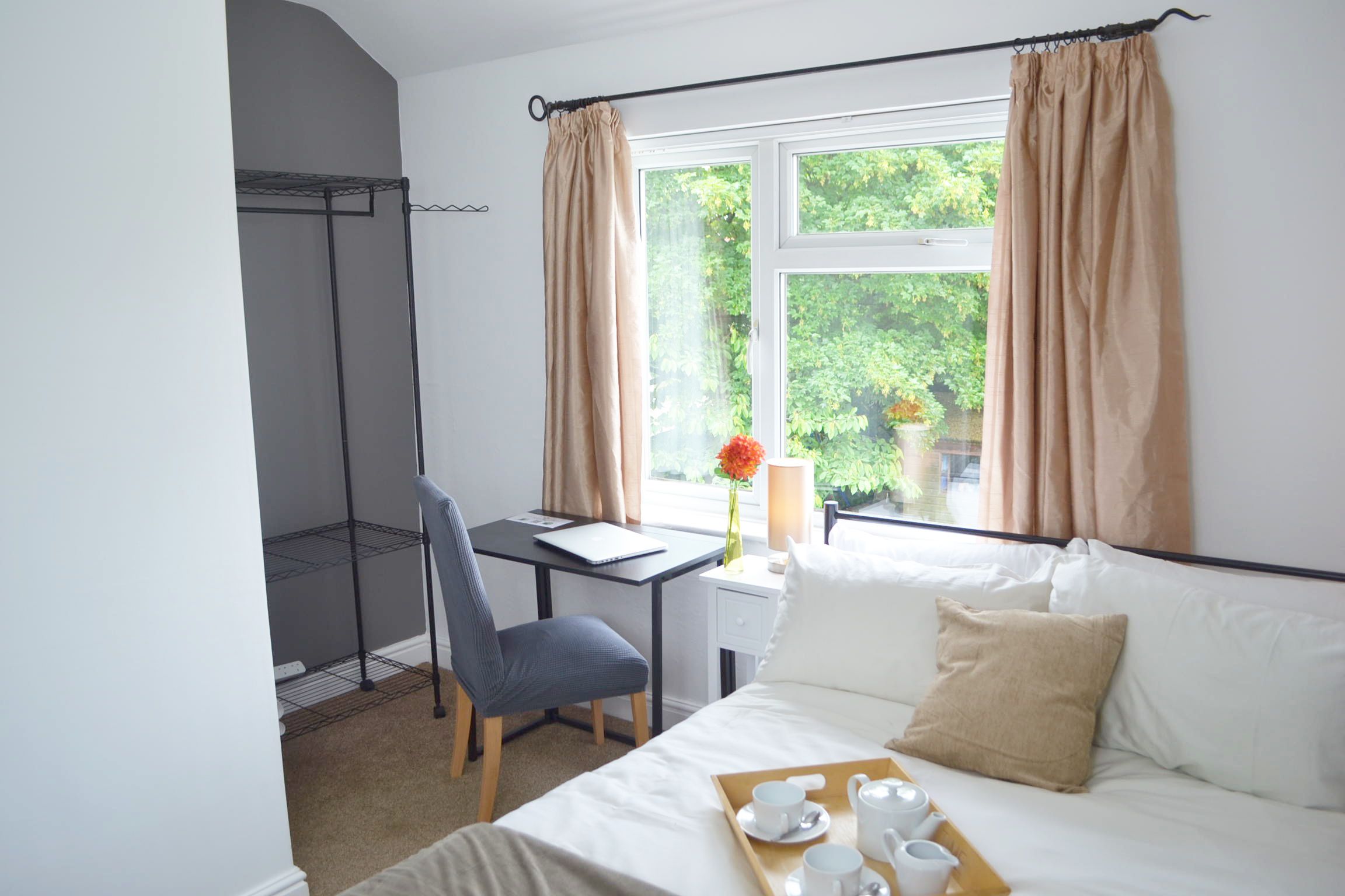 Une chambre d’hôtel avec un lit, un bureau, une chaise, une fenêtre avec des rideaux et une vue sur la verdure.