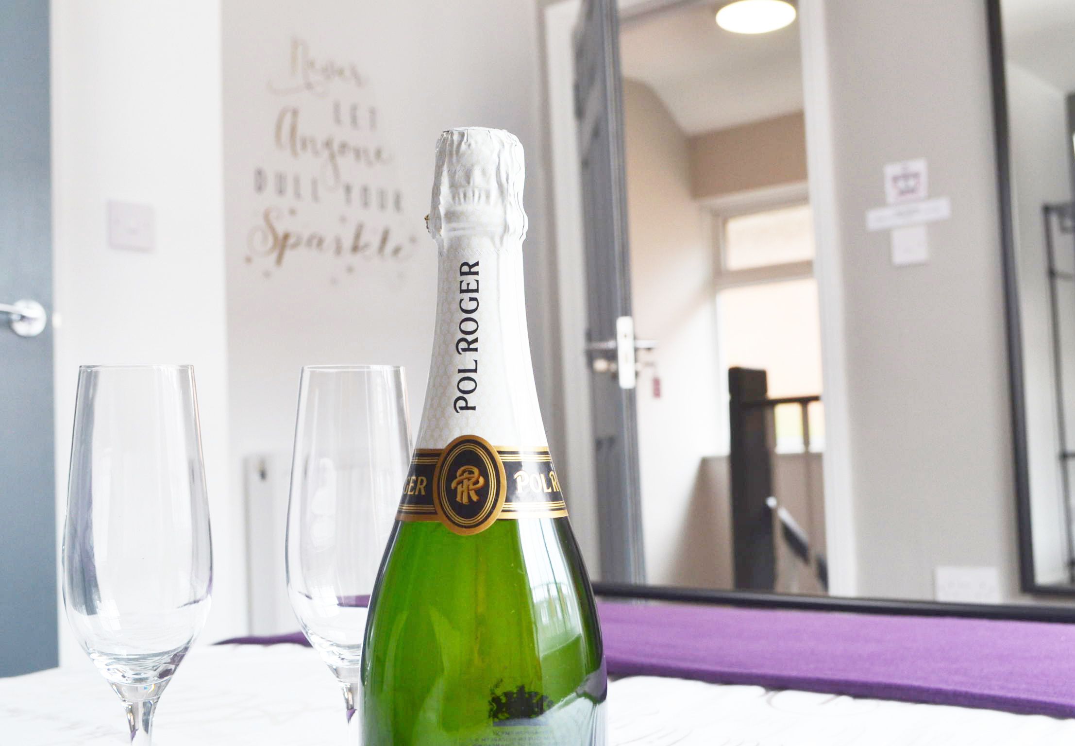 Una botella verde de champán Pol Roger con dos copas vacías sobre una mesa.