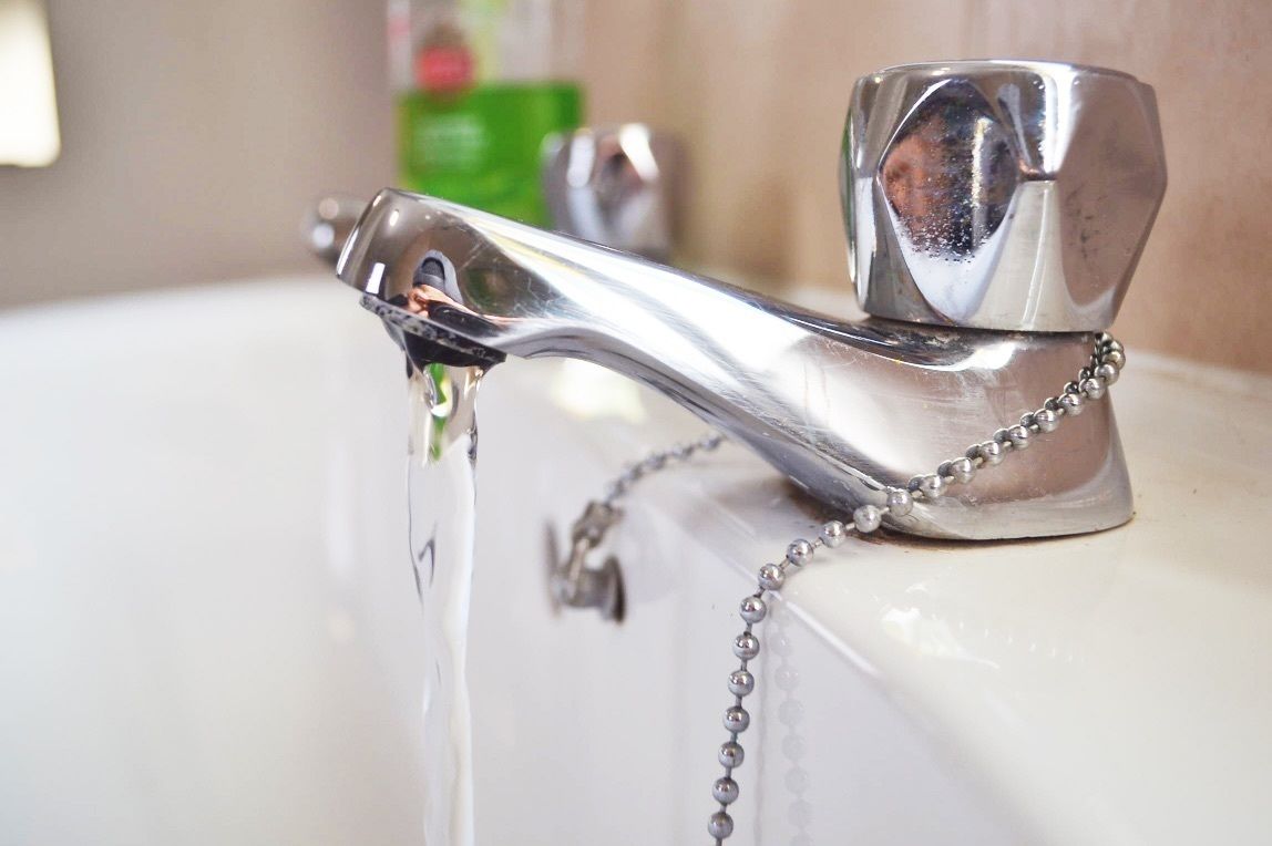 A chrome faucet with water running, attached to a white sink.