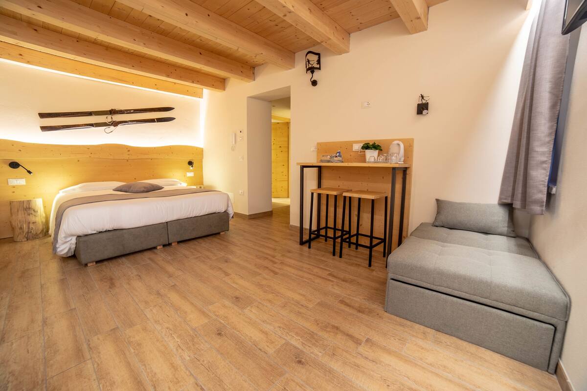 A bedroom with a bed, a sofa, a wooden table, and a ski rack.