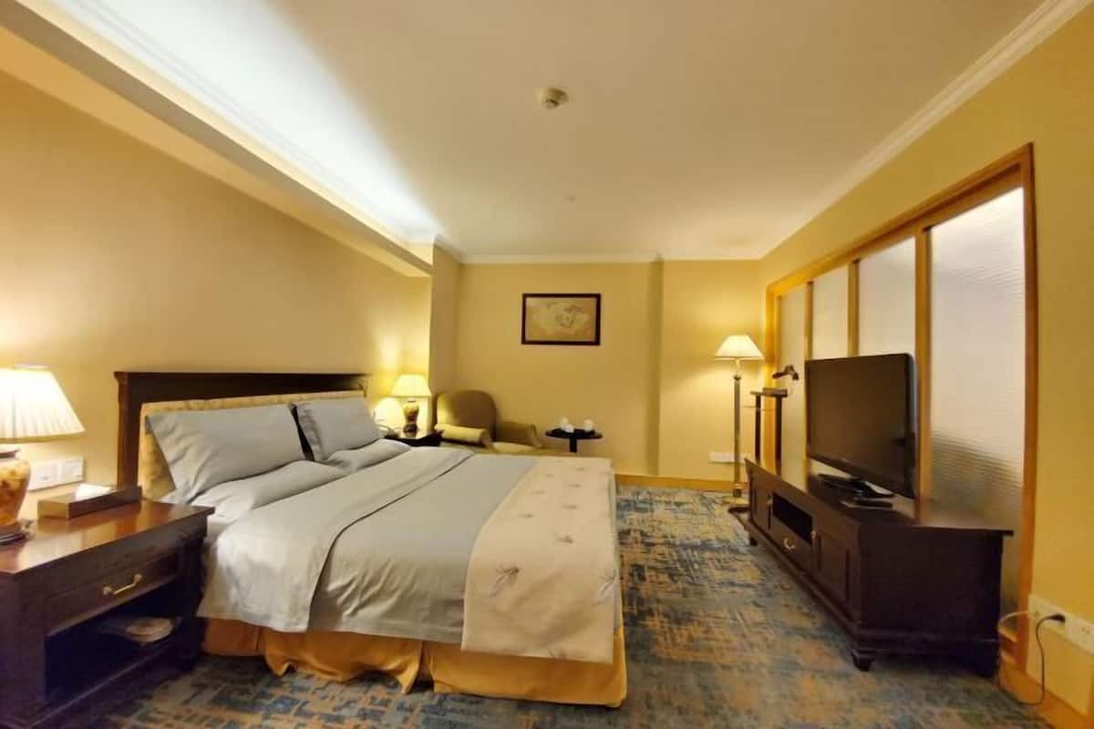 A hotel room with a bed, bedside table, lamp, chair, TV, and a carpeted floor.
