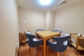 A small dining area with a wooden table and four chairs, a small shelf with a teapot, and a light fixture on the ceiling. - Zhongtian Huanghai Hotel (Rudong)