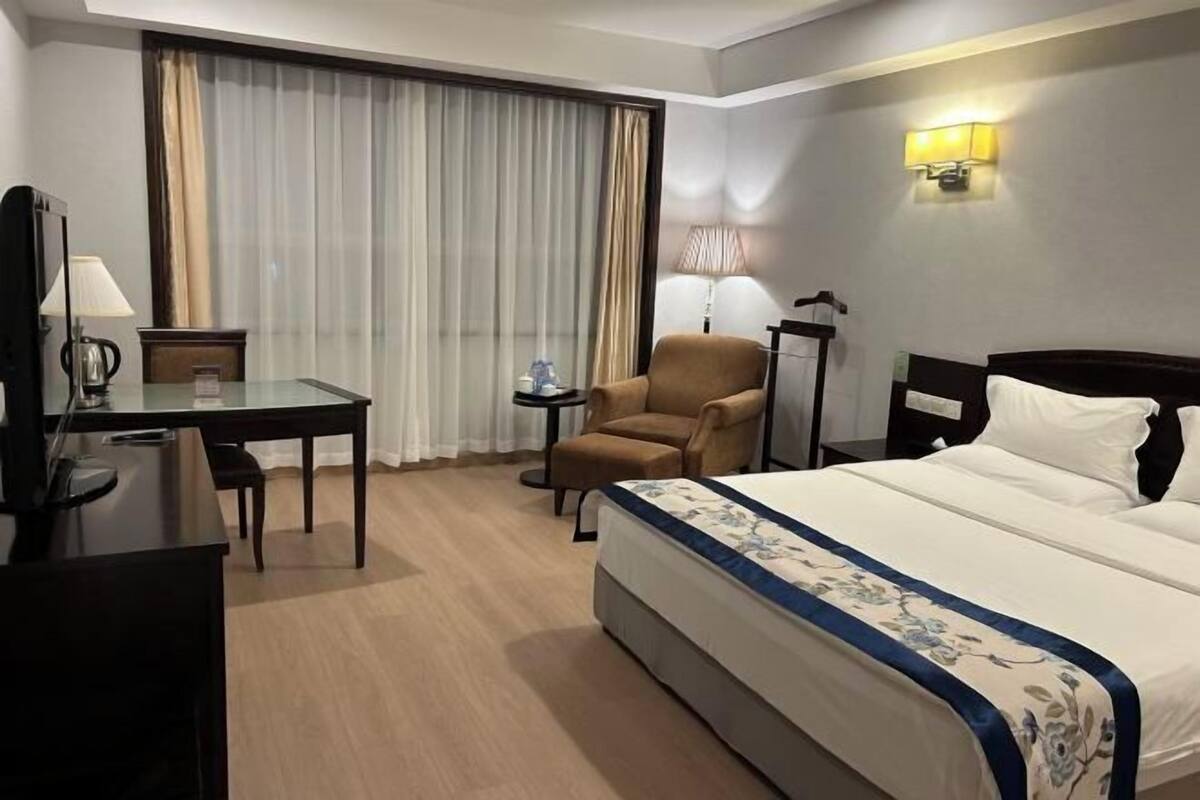 A hotel room with a bed, a desk, a chair, a TV, and a window with curtains.