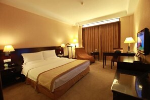 A hotel room with a large bed, a desk with a chair, a television, and a window with curtains. - Zhongtian Huanghai Hotel (Rudong)