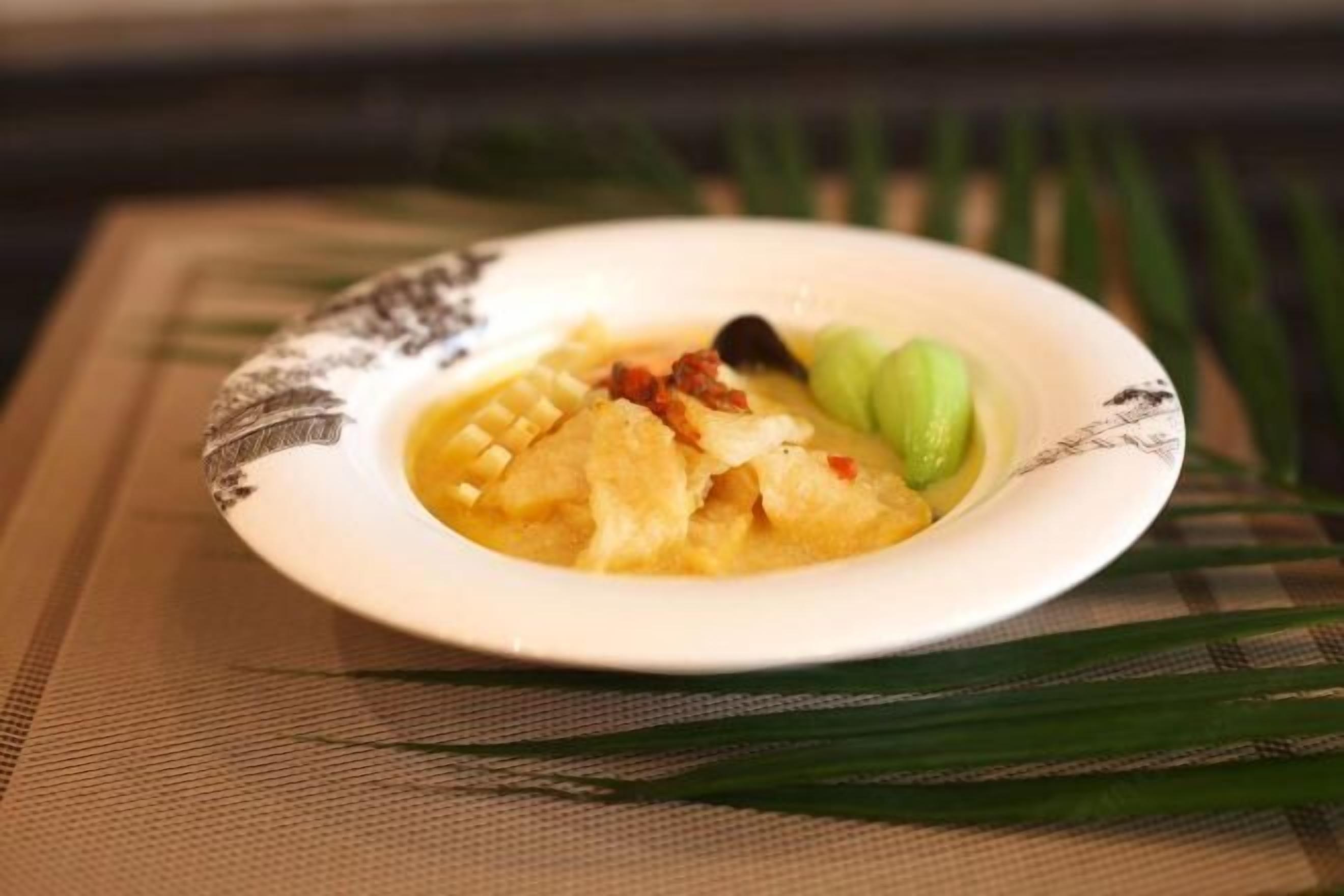 A bowl of soup with vegetables and a piece of meat on a placemat.
