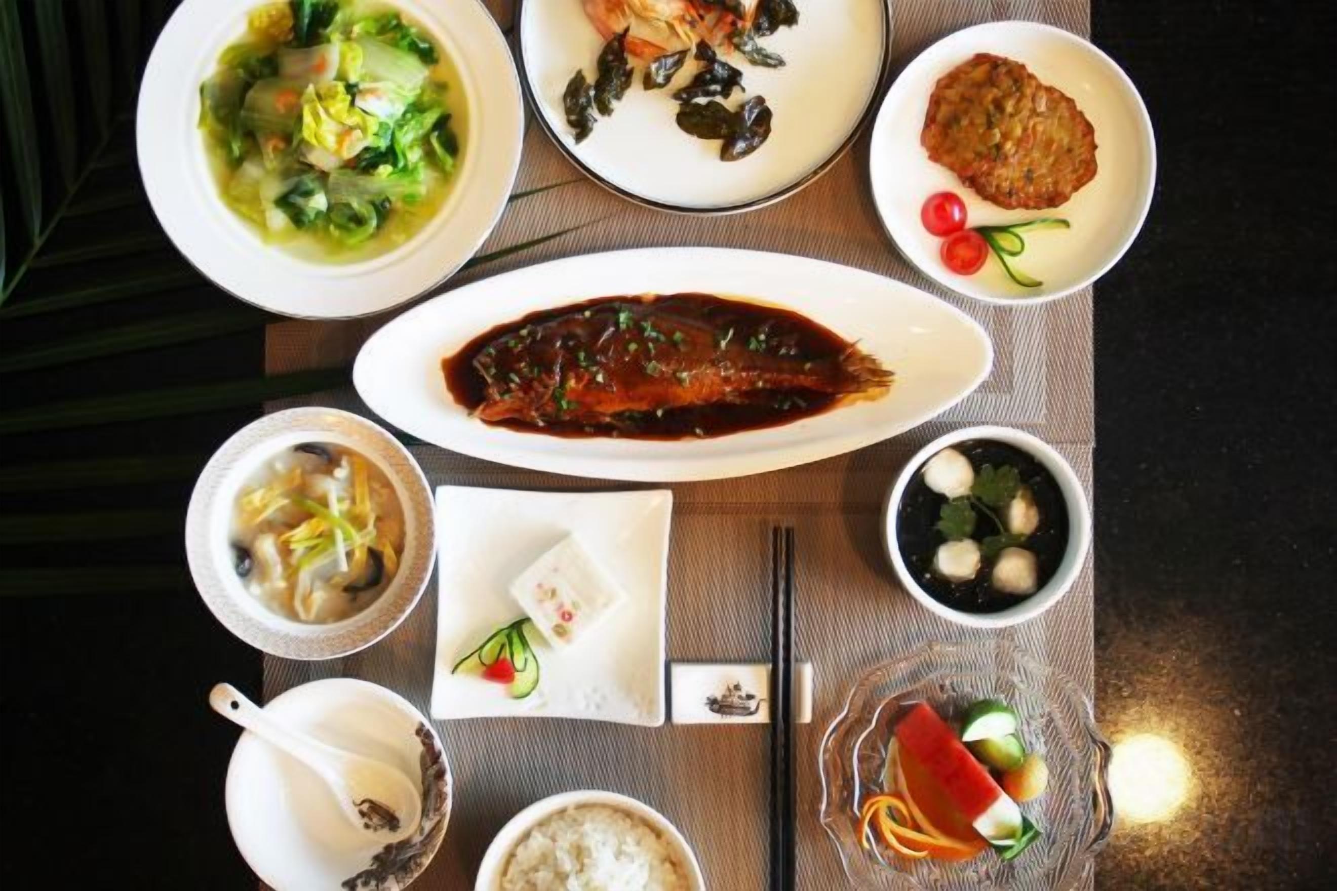 A variety of dishes on a table, including a bowl of soup, a plate of meat, and a dish with a dark sauce.