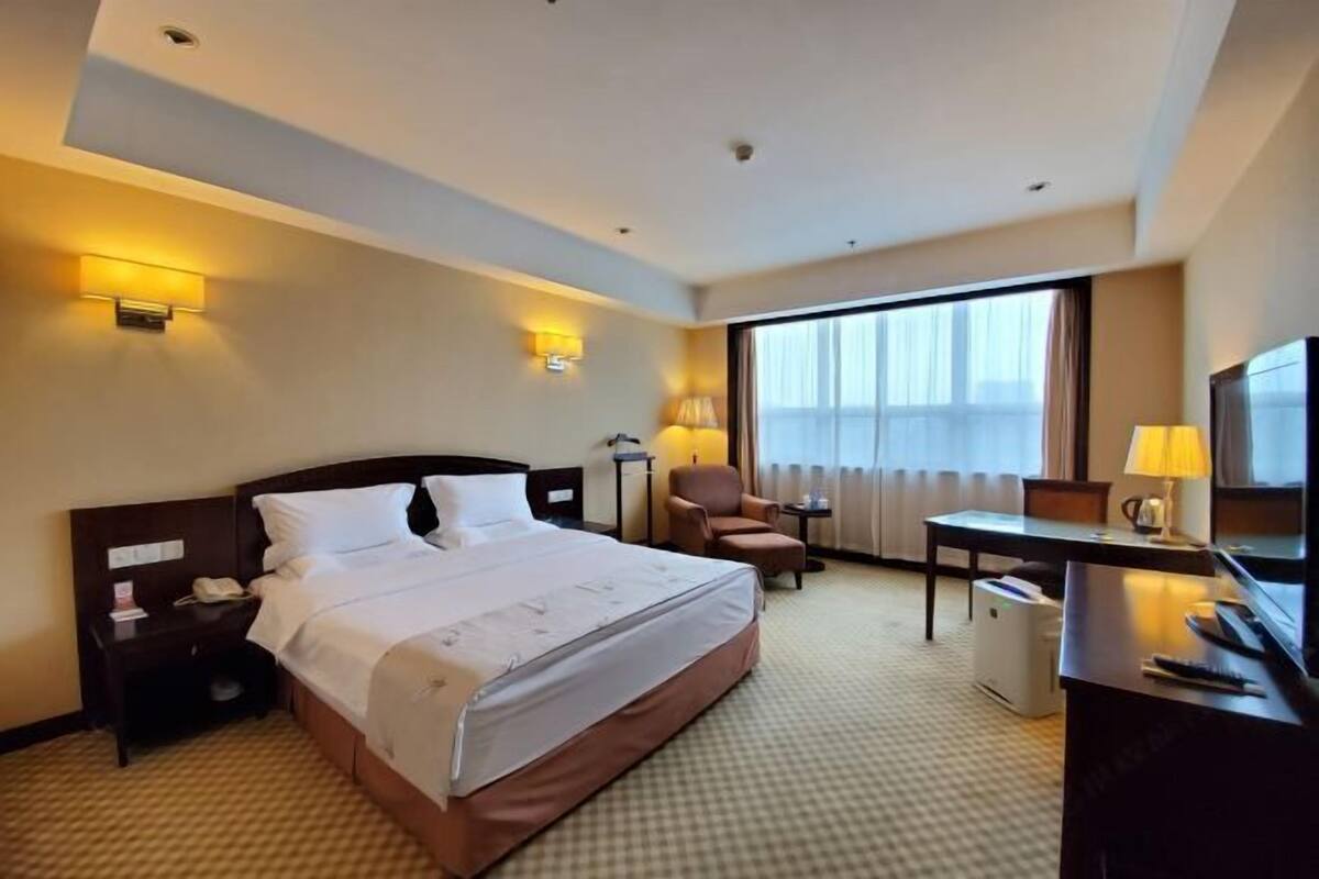 A hotel room with a large bed, a desk, a chair, and a TV.