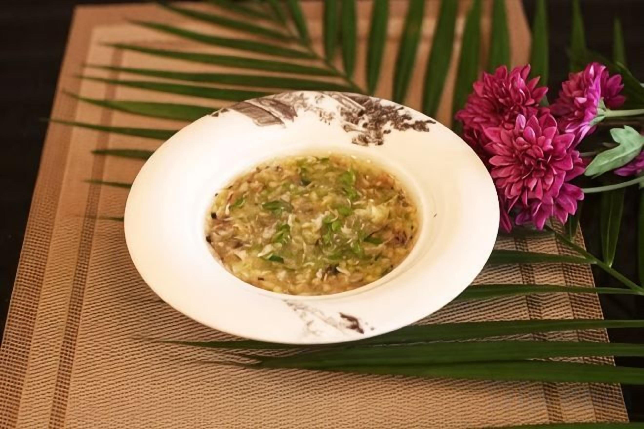 A bowl of soup on a table with a placemat and flowers.