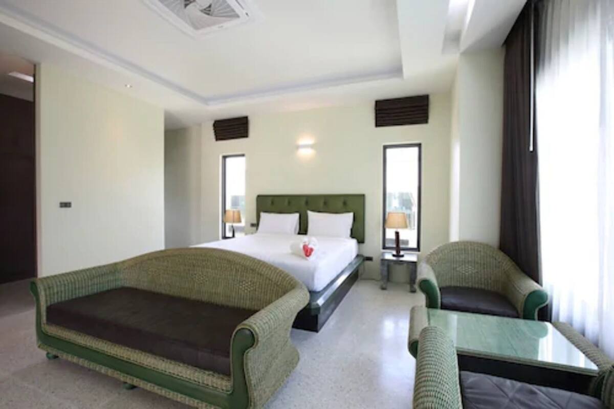 A hotel room with a bed, a green sofa, a small table, and a window with curtains.
