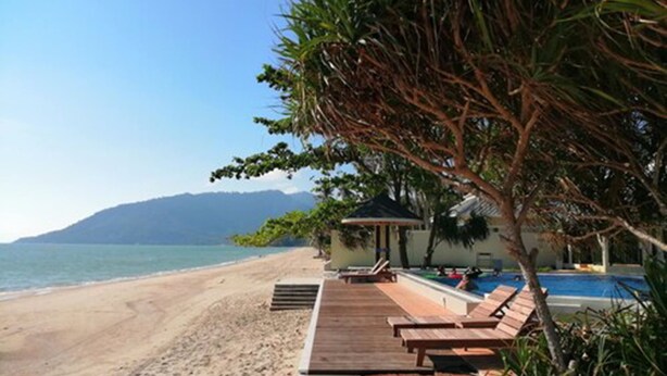 Una playa con una terraza de madera, sillas de descanso y zona de piscina.
