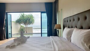Habitación de hotel con una cama grande, vista al océano y un balcón con un árbol.