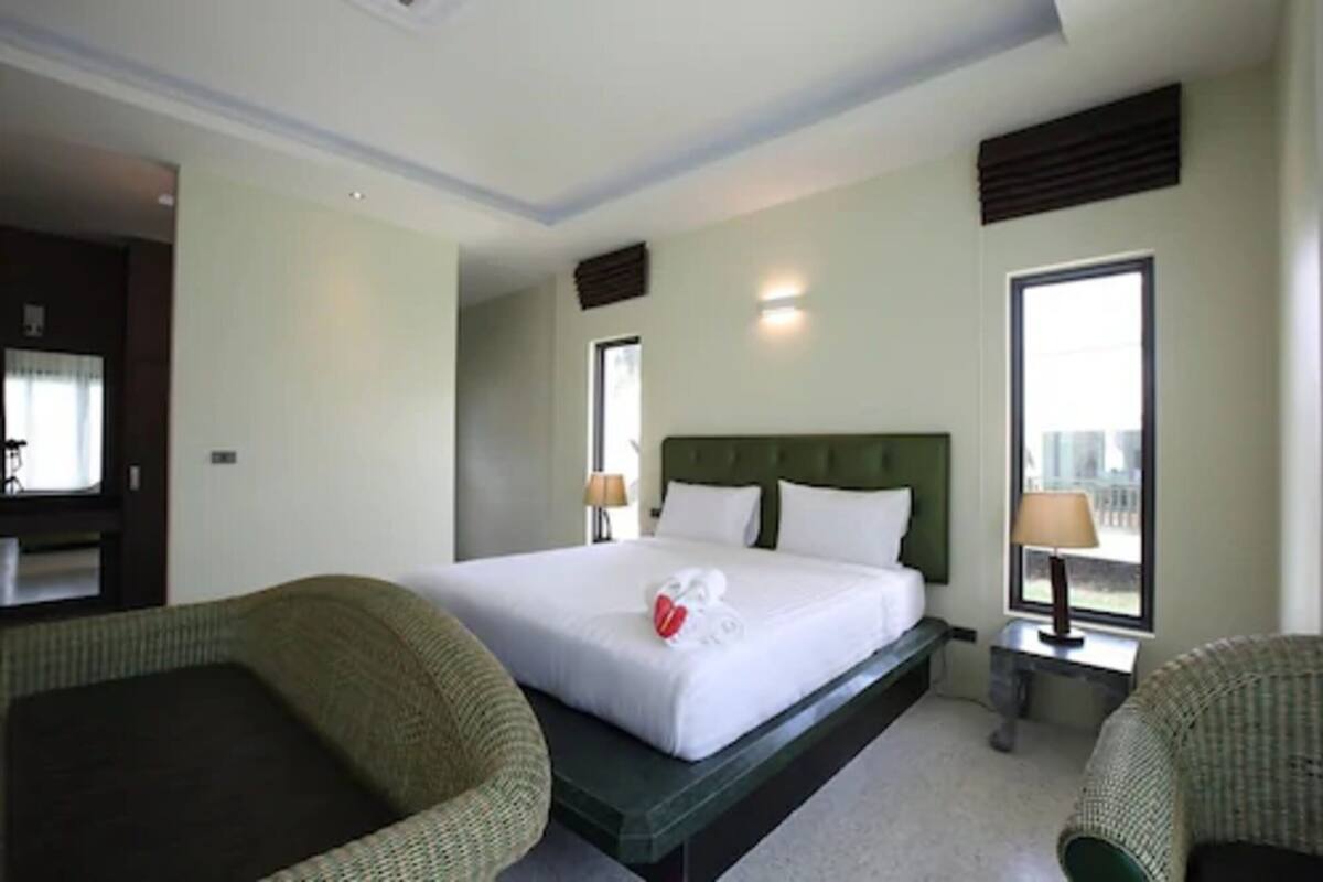 A hotel room with a large bed, two bedside tables, a green upholstered chair, and a window providing a view.