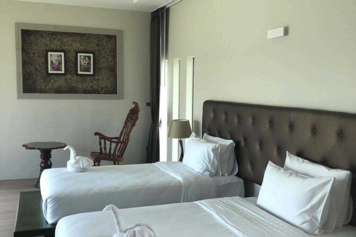 A hotel room with two beds, a chair, a small table, and a wall-mounted picture.