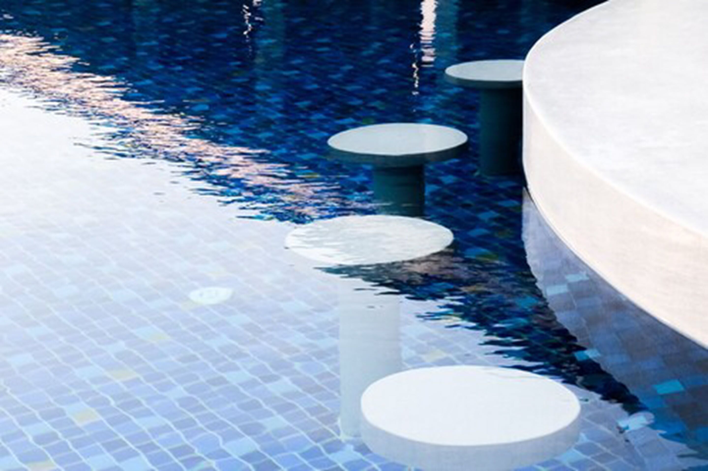 Área da piscina com piso ladrilhado e assentos circulares ao redor.