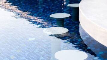 Área da piscina com piso ladrilhado e assentos circulares ao redor.
