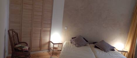 A bedroom with a bed, two bedside tables, a chair, a wardrobe, and a small table with a lamp.