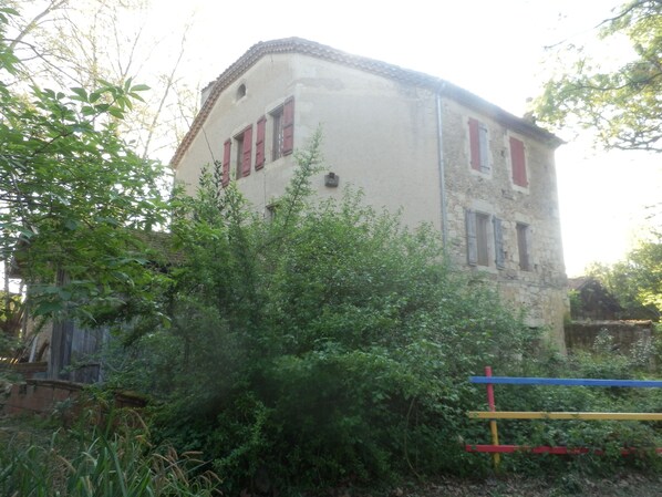 Un bâtiment à deux étages avec des volets rouges, entouré d’une végétation luxuriante.
