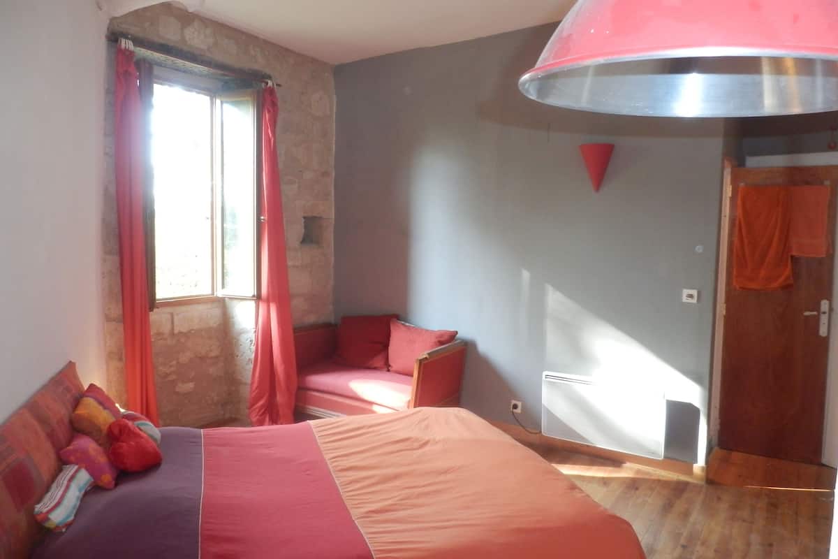 Un dormitorio con cama, una ventana con cortinas, una silla roja y una puerta.