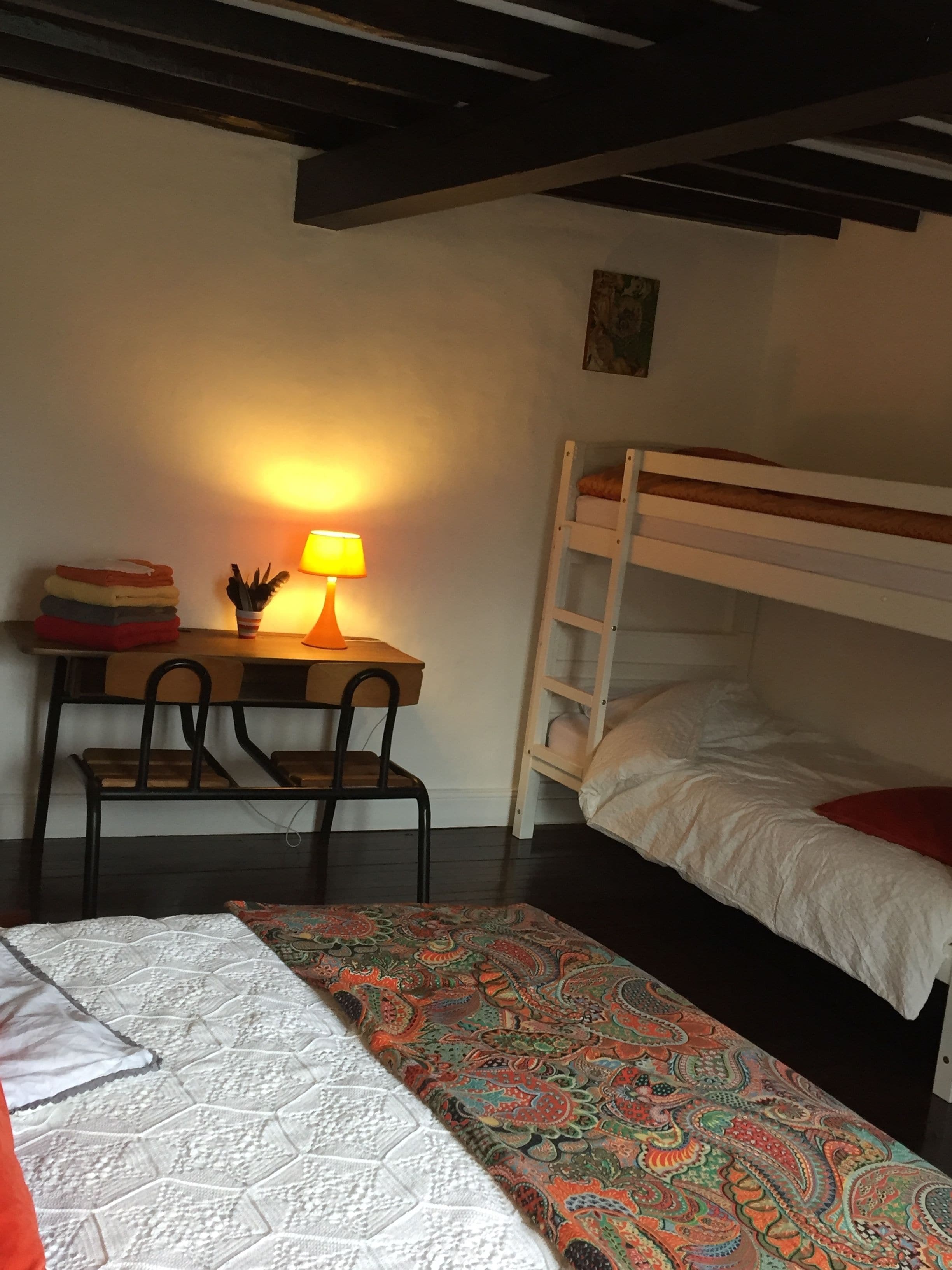Una habitació de dormitori amb un llit superposat, un escriptori amb una làmpada, una cadira i una catifa amb disseny.