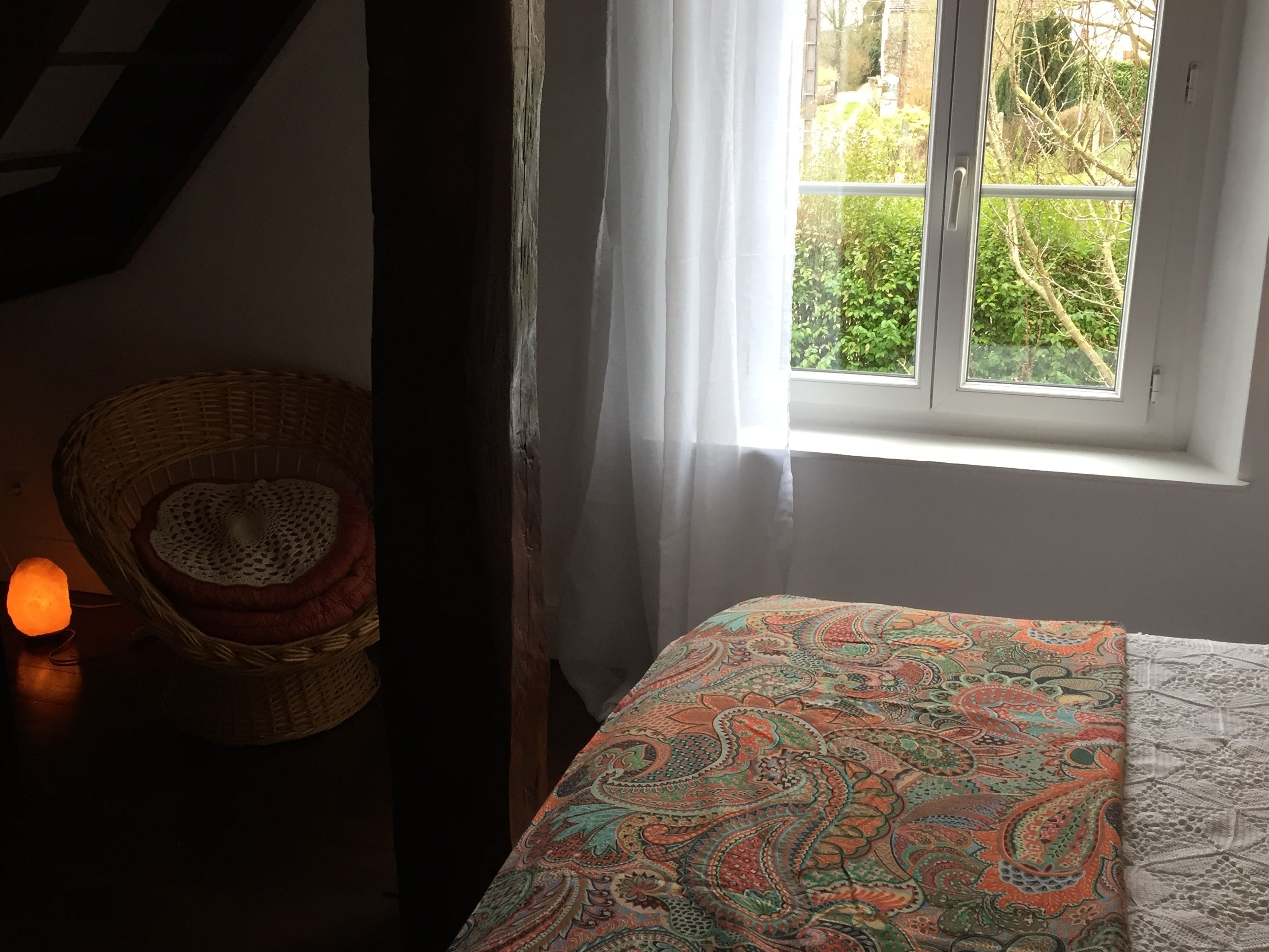 A bedroom with a bed, a window with curtains, a chair, and a lit lamp.