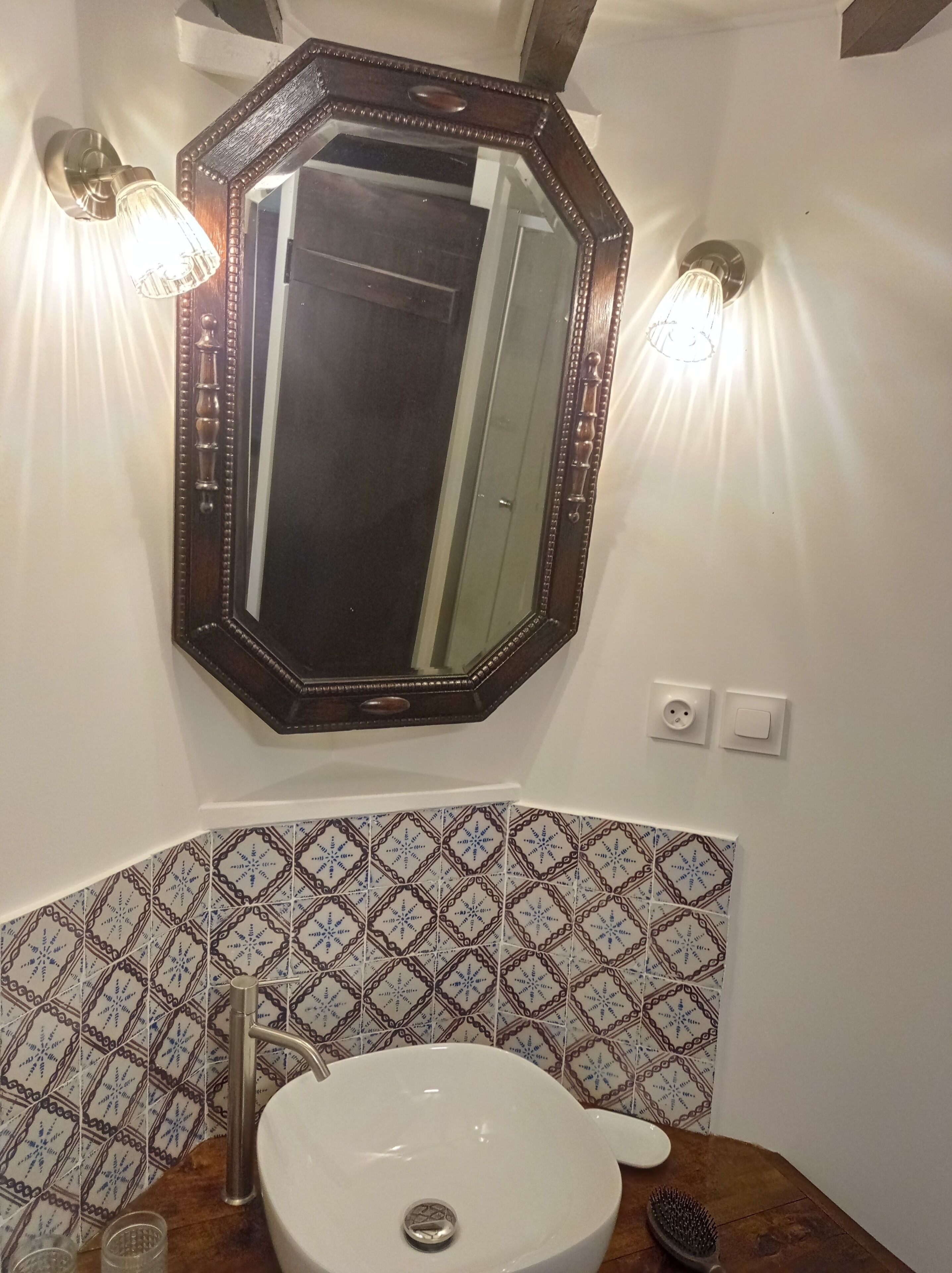 A bathroom with a large mirror, two wall-mounted lights, a sink, and patterned tiles.