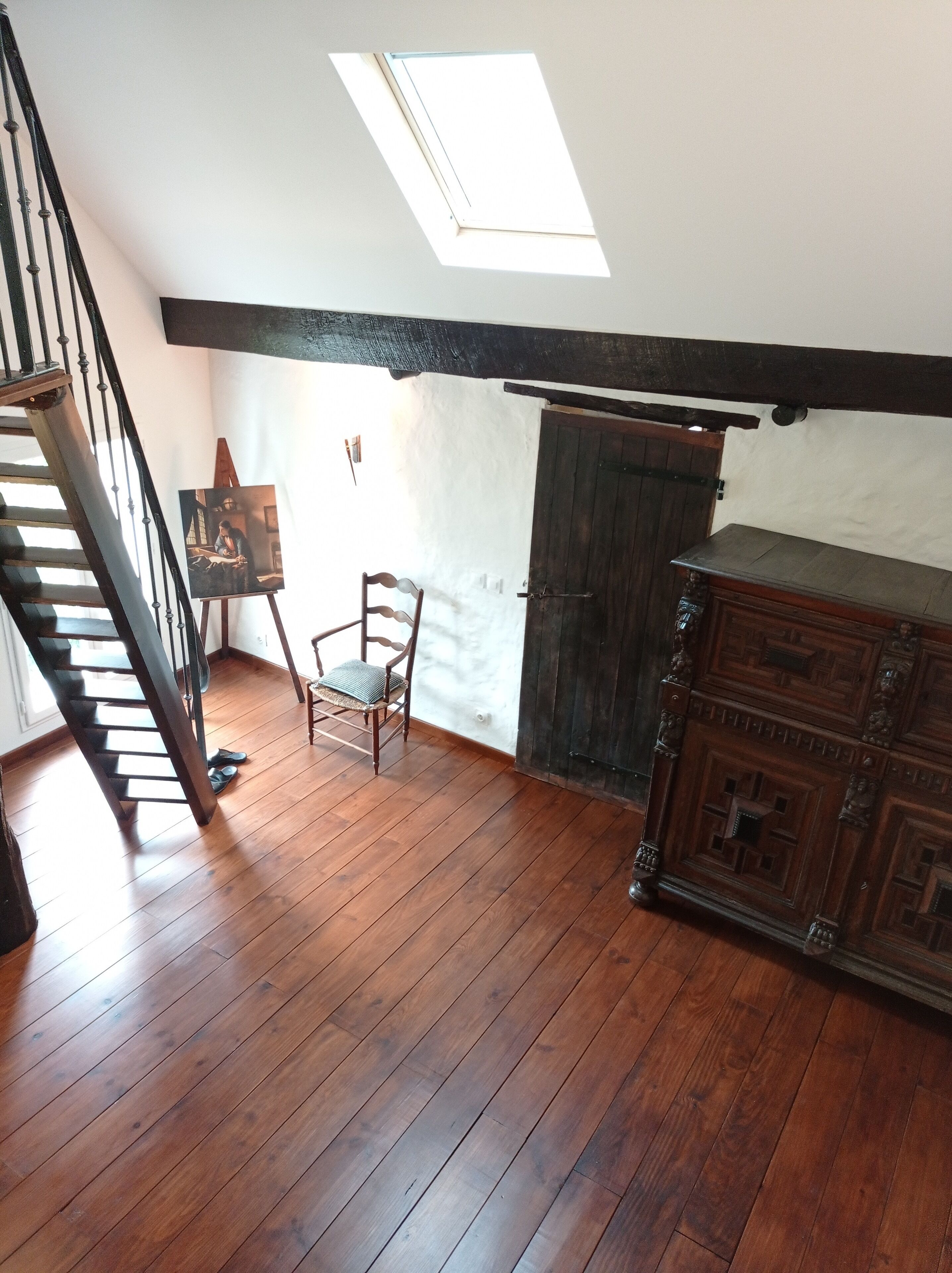 A room with a wooden floor, a staircase, a skylight, a chair, and a wooden cabinet.