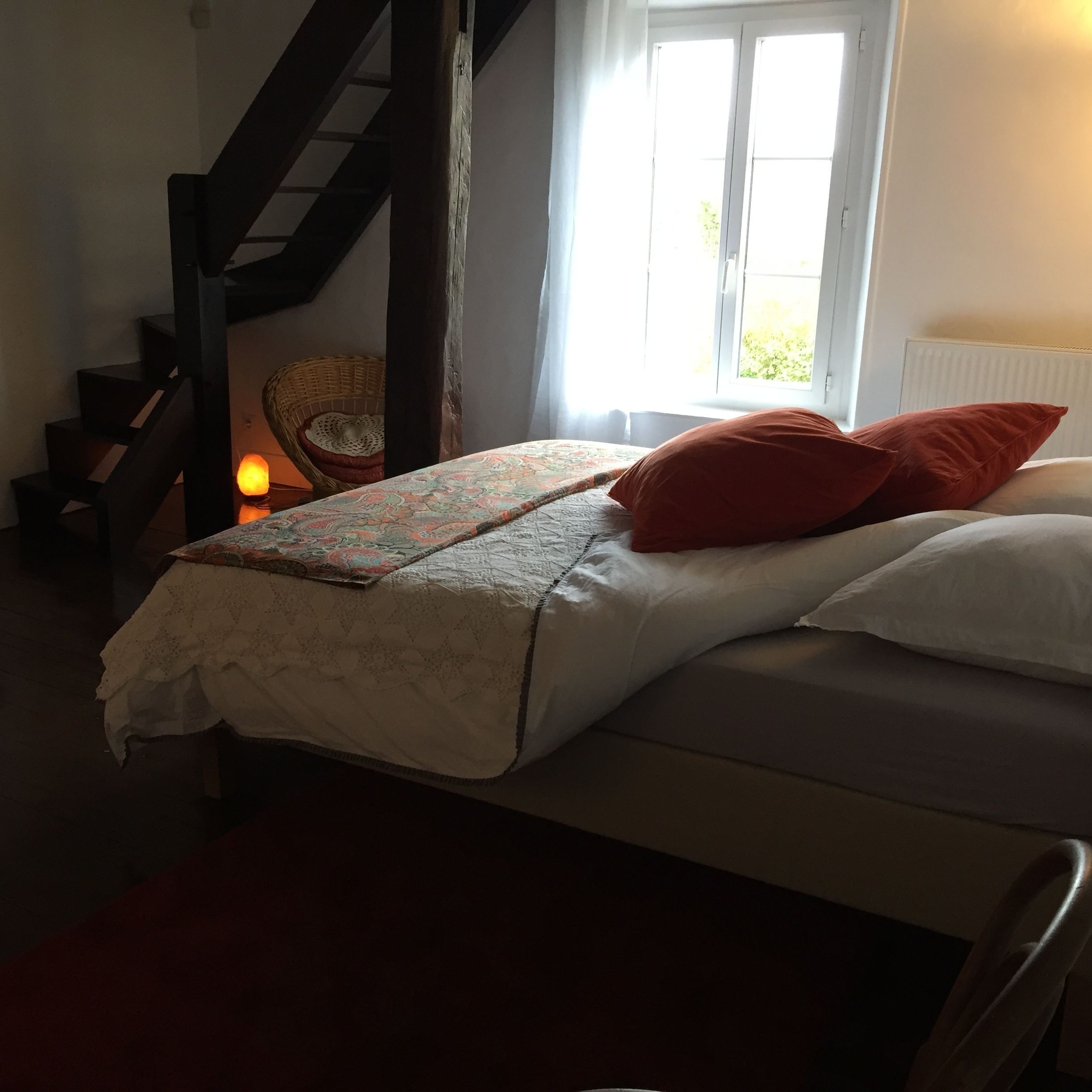 A bedroom with a bed, a chair, a window, and a staircase.
