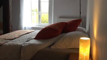 Een slaapkamer met een bed, kussens, een bedlampje, een raam en een radiator.