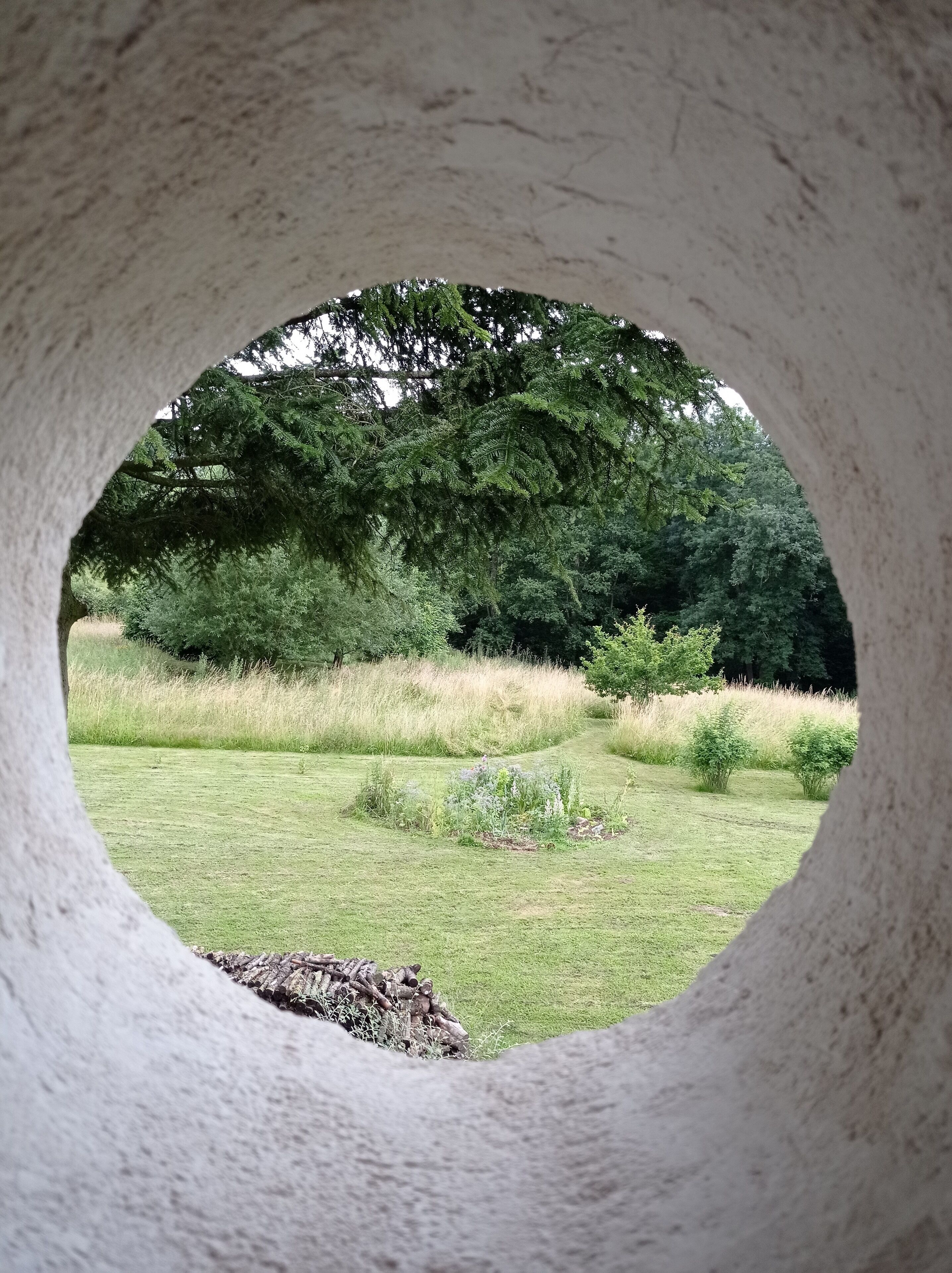 Una abertura circular con vista a un campo cubierto de hierba y árboles al fondo.