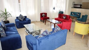 A modern living room with blue and red sofas, a glass coffee table, and a yellow ottoman. - Boutique Hôtel Albaraka (Dakhla)