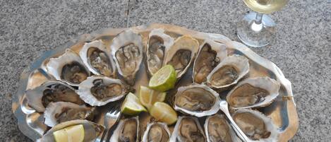 A plate of oysters with lime wedges and a glass of white wine on a granite countertop.