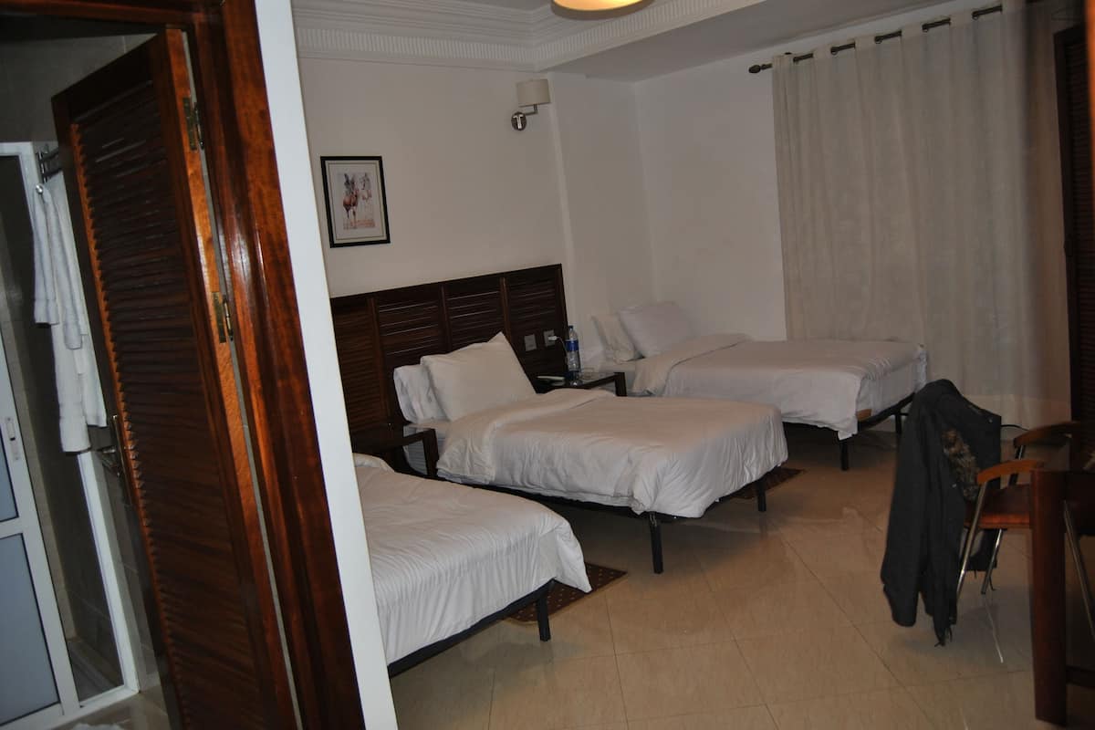 A hotel room with three single beds, a wooden door, a white wall with a framed picture, and a curtain.