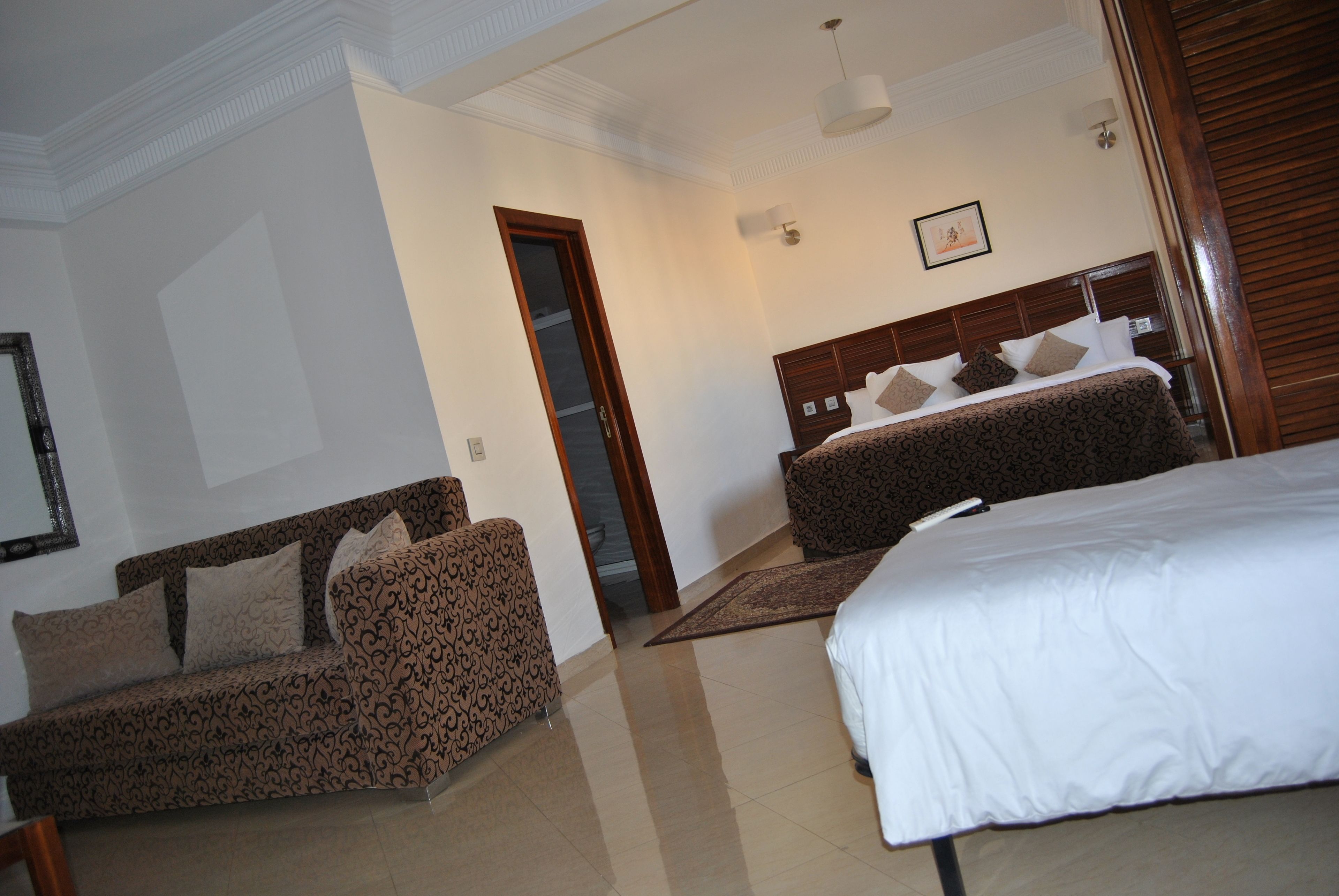 A hotel room with a large bed, a sofa, a wooden headboard, and a door leading to another room.
