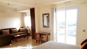 A hotel room with a large bed, a sofa, a desk, and a chair. There is a balcony with a view. - Boutique Hôtel Albaraka (Dakhla)