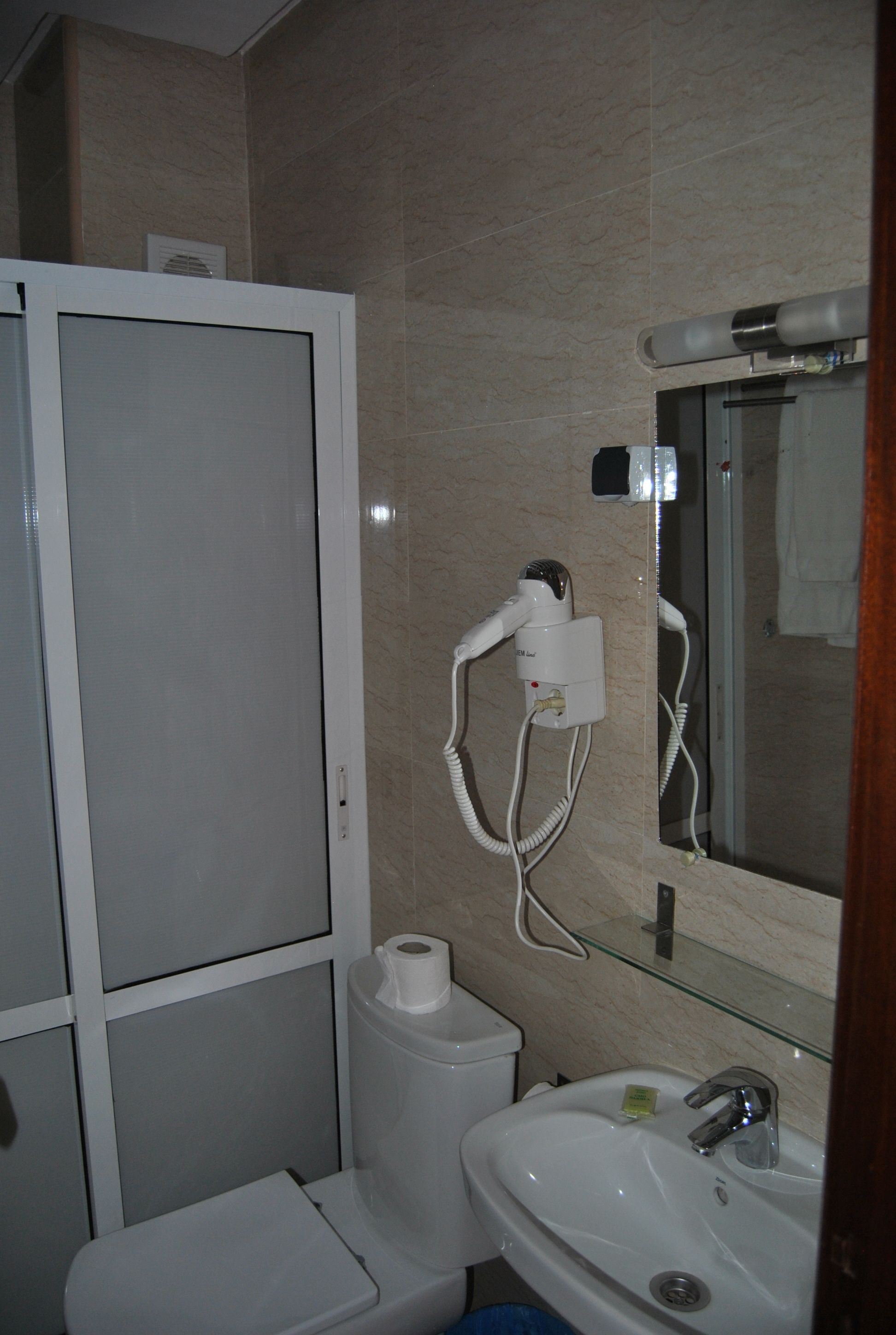 A bathroom with a toilet, sink, and a hairdryer mounted on the wall.