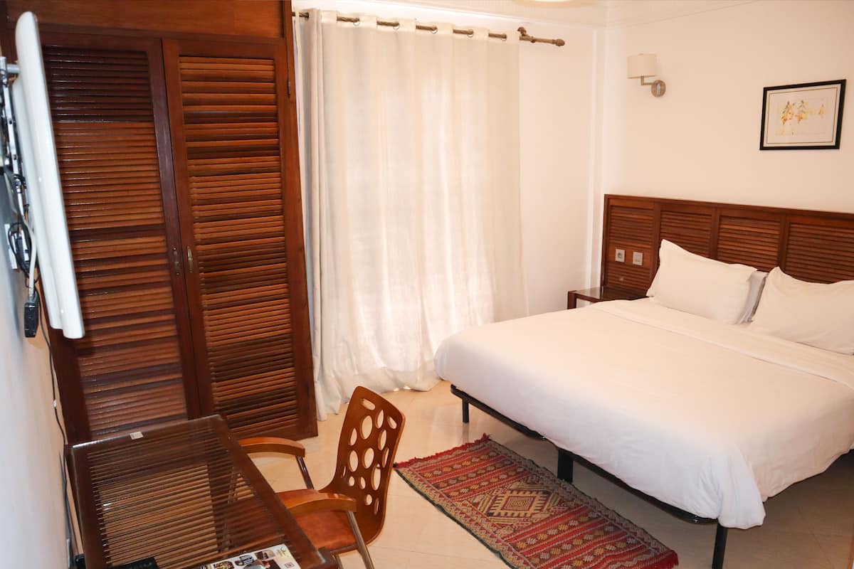 A bedroom with a wooden headboard, a single bed, a chair, a desk, and a patterned rug.