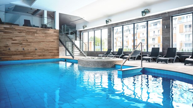 Une piscine intérieure avec un mur en bois, des chaises longues et un jacuzzi.