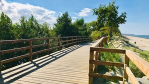 Une promenade en bois menant à une plage, avec un ciel dégagé et des arbres.
